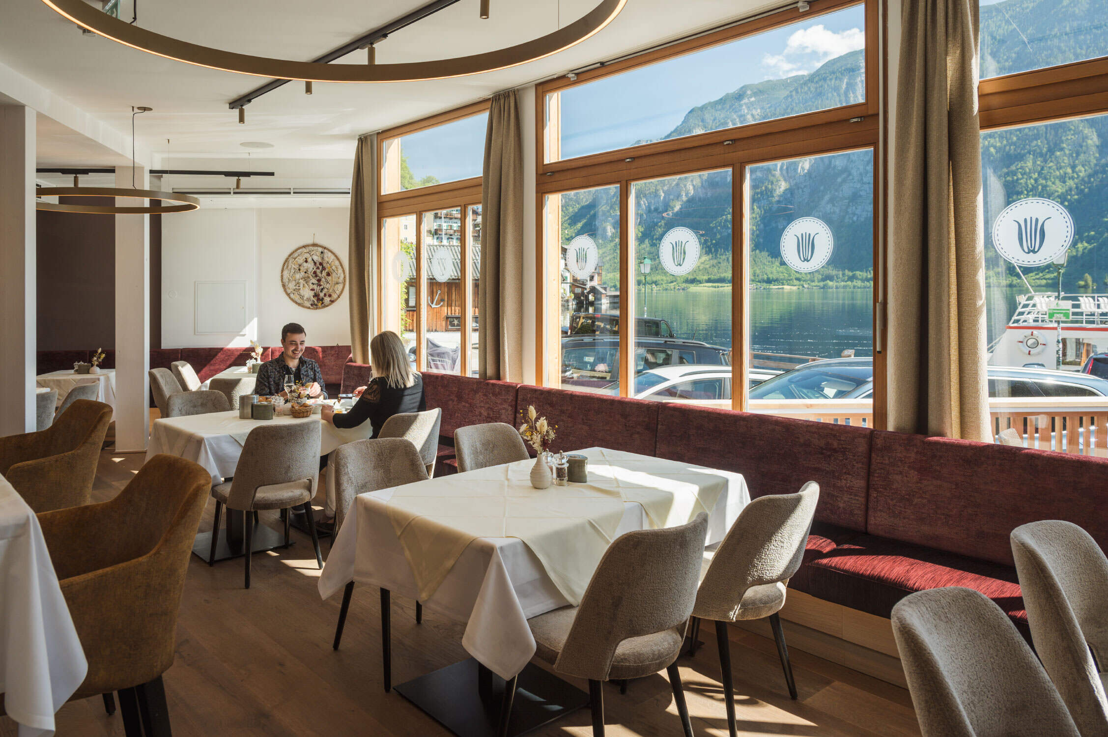 Ein Pärchen sitzt an Tischen in einem Restaurant und genießt das traumhafte Panorama im Herzen des Salzkammerguts.